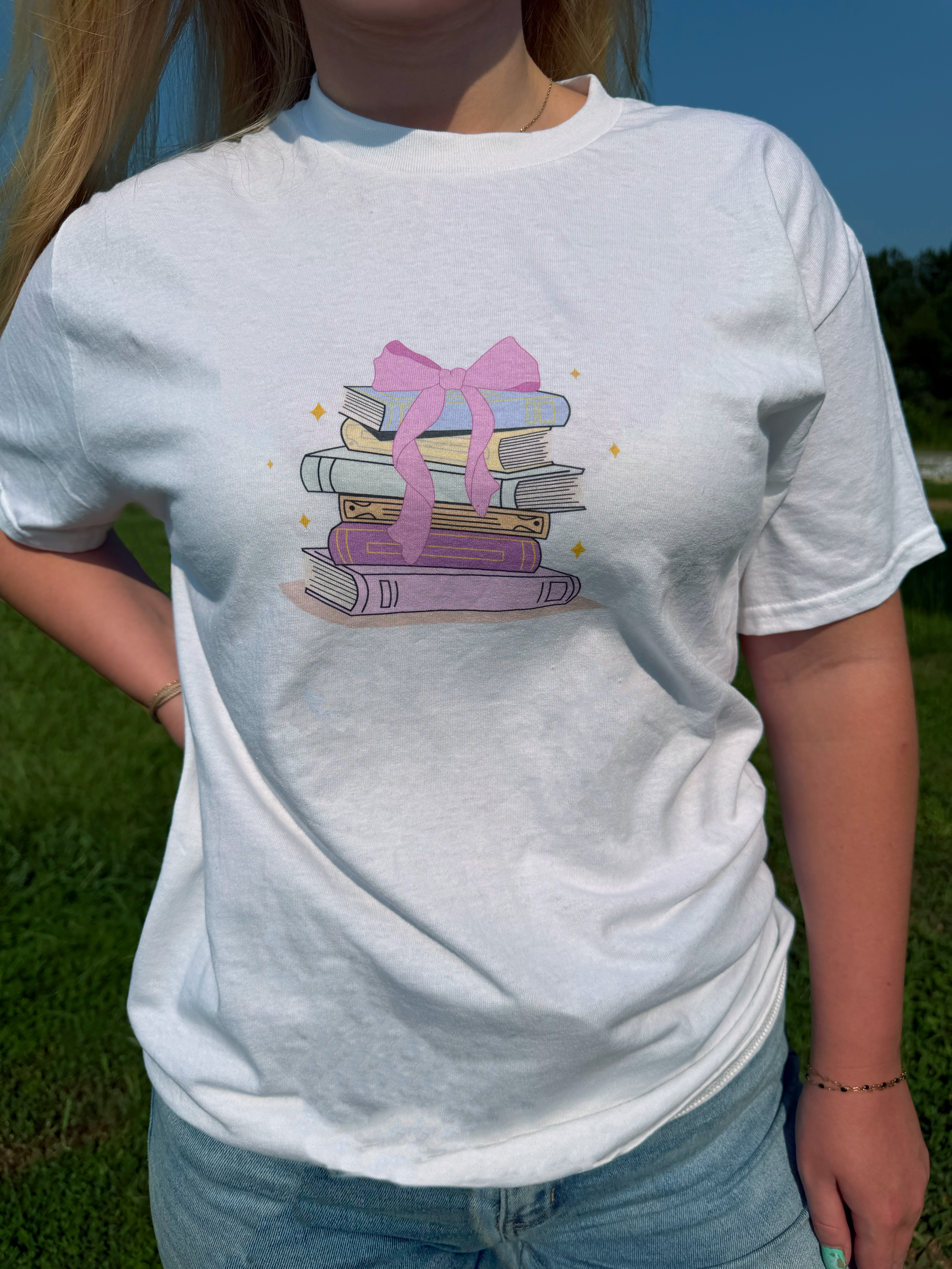 White T-shirt with a DTG print of stacked books tied with a pink bow